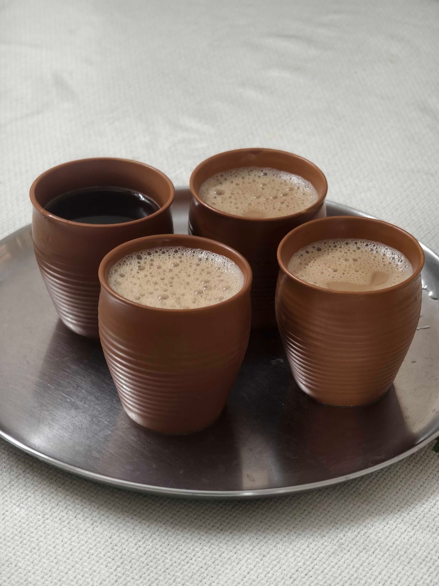 Four clay kulhads of chai on a tray, seen from above