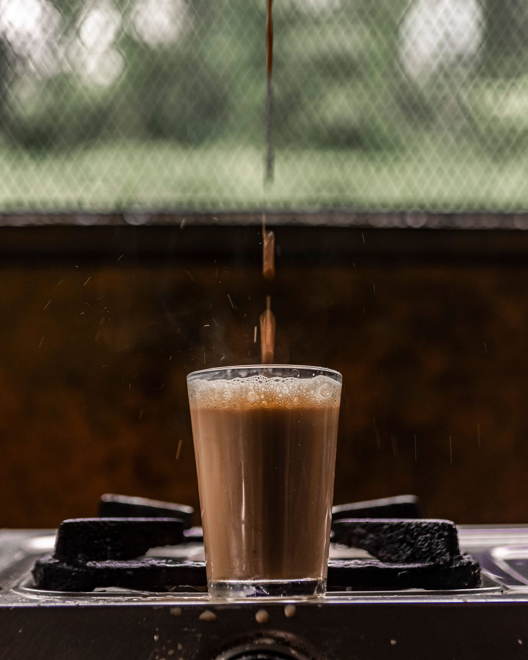 Milk chai coming to a boil on the stove, steam rising off the glass